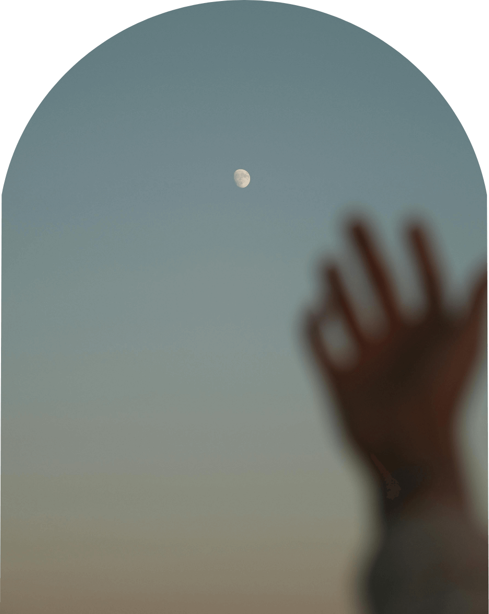 夕暮れの空に浮かぶ月に向かって手を伸ばすシルエット