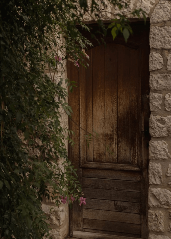 石壁に囲まれた木製のドアと緑の葉、花が垂れるエントランス